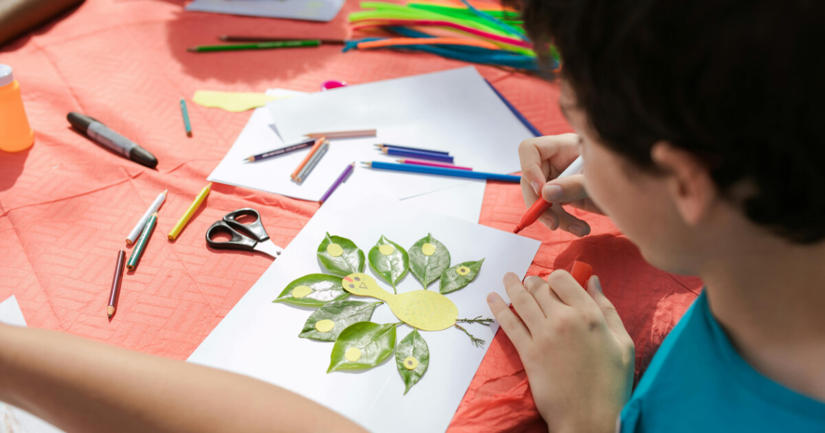 Child creating an art piece using leaves and crayons during a craft session outdoors
